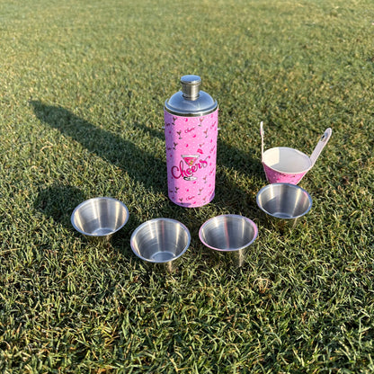 Pink flask bottle with silver shot glasses on green grass